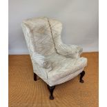 A George II style carved walnut wing back arm chair, with beige upholstery,