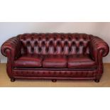 A red leatherette three seater Chesterfield settee, with button back upholstery,