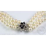 A three strand cultured pearl necklace with sapphire and diamond set white meatl foliate clasp