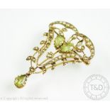 An Edwardian peridot and split seed pearl set brooch/pendant, of typical sinuous form,