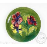 A Moorcroft hibiscus pattern plate, decorated with three blooms against a green ground,