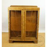 A late Art Deco walnut display cabinet, with two 'sunray' glazed doors on bracket feet,