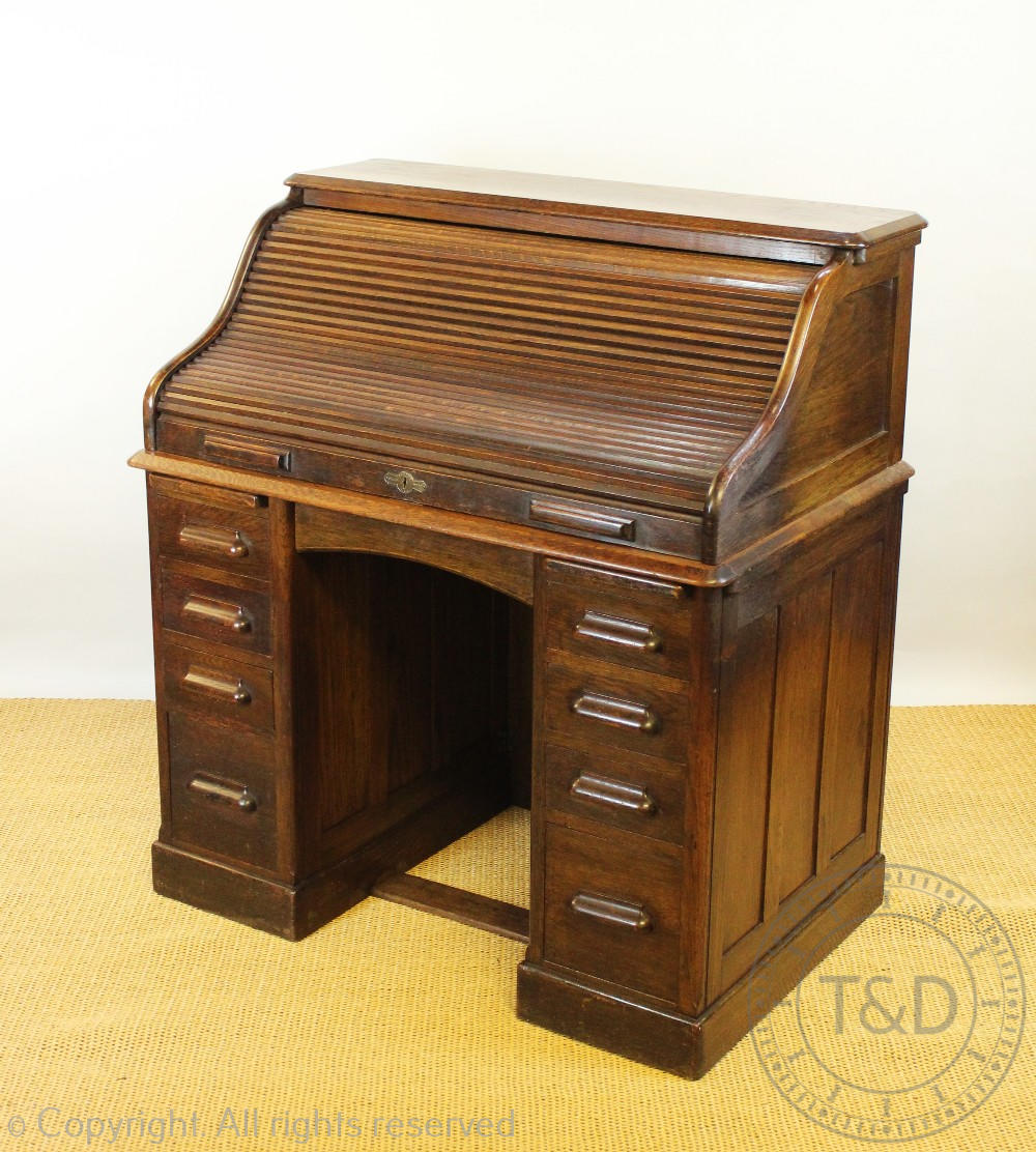 An Edwardian oak roll top desk, with tambour above an arrangement of nine drawers, on plinth base,