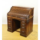 An Edwardian oak roll top desk, with tambour above an arrangement of nine drawers, on plinth base,