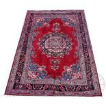 A Persian Meshad type wool carpet, worked with a floral medallion against a red ground,