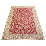 A Persian Tabriz wool carpet, worked with an all over floral design against a red ground,