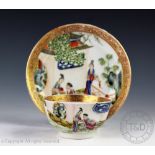 An 18th century style tea bowl and saucer, each decorated with figures on a veranda,