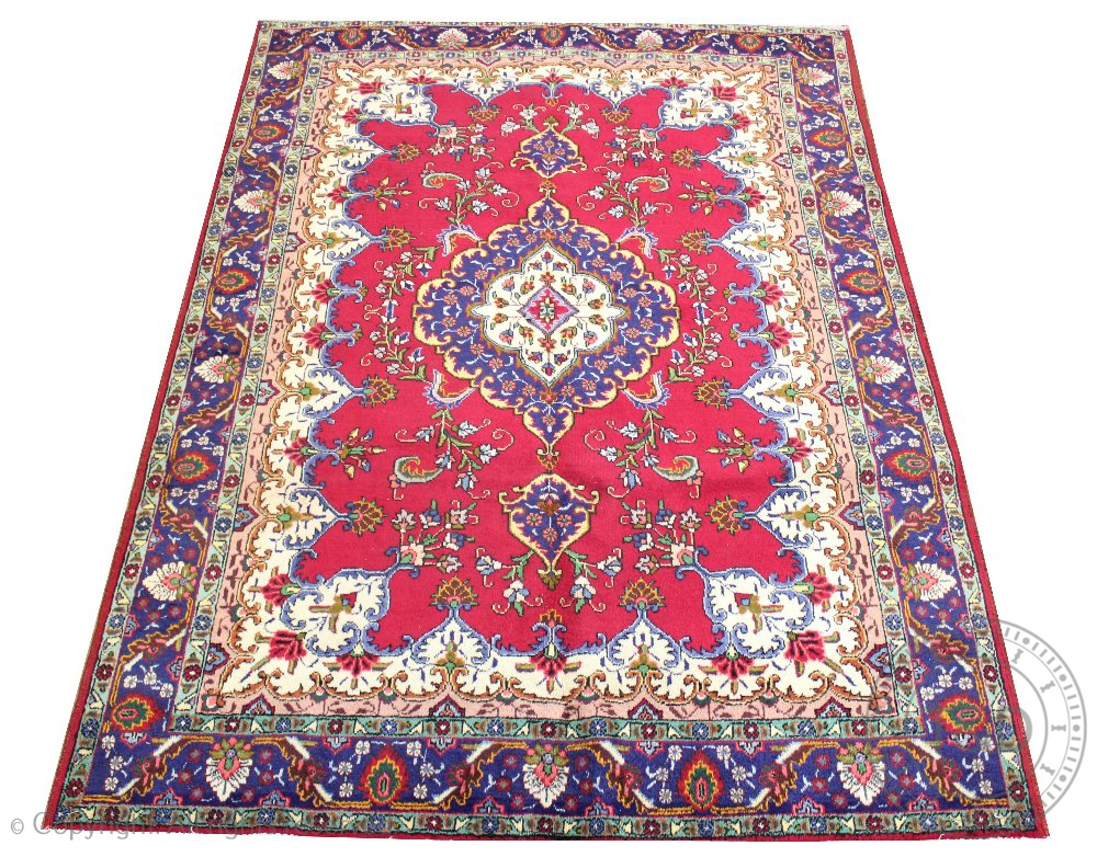 A Persian wool carpet, worked with a central blue medallion and floral motifs against a red ground,