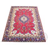 A Persian wool carpet, worked with a central blue medallion and floral motifs against a red ground,