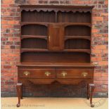 A George III style oak dresser, the raised back with six shelves and a cupboard door,