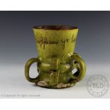 A Ewenny pottery cup in green glaze with loop handles inscribed 'Gwappau Yr Hen Cymru Yr 1677/a cup