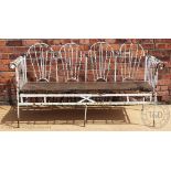 A wrought iron garden bench, possibly French, the four section arched back with brass finials,