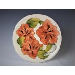 A Moorcroft Hibiscus pattern circular plate, decorated with orange buds against an ivory ground,