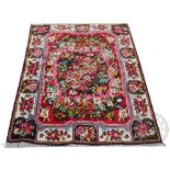 A Persian full pile wool rug, worked with a central floral spray,