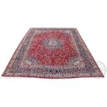 A Persian Kashan wool carpet, worked with a central blue medallion against a floral red ground,