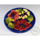 A Moorcroft Hibiscus pattern plate, decorated against a blue ground,