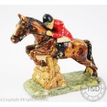 An early 20th century pottery model of a huntsman jumping, on a grass base,