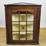 A George III oak hanging corner cabinet, with glazed door enclosing serpentine shelves,