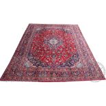 A Persian hand woven wool carpet, worked with a central blue medallion against a foliate red ground,