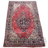 A Persian hand woven wool rug, worked with a floral design against an abrashed red ground,