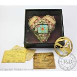 A World War One heart shaped pin cushion, set with glass beads, badges etc,in an ebonised case,