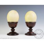 A pair of 19th century ostrich eggs on stands, each egg on a turned mahogany stand, 26.