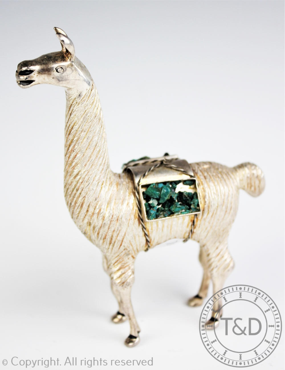 A white metal model of a Llama, modelled standing with green stone set paniers,