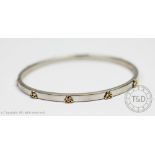 A white gold bangle, the hinged bangle set with eight yellow gold Celtic knots throughout,