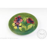 A Moorcroft hibiscus pattern plate, decorated with three blooms against a green ground,
