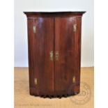 A George III mahogany bow front hanging corner cabinet, with fluted sides and scroll apron,