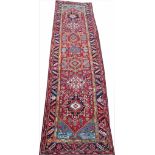 A Persian Heriz hand woven wool runner, worked with six floral rulls against a red ground,