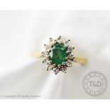 An emerald and diamond oval cluster ring, the oval emerald surrounded by twelve diamonds,