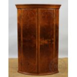 A George III style bow front corner cupboard, the walnut cupboard with satinwood inlay,