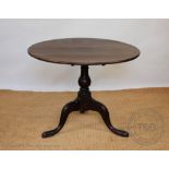 A George III oak tilt top circular table, with turned column with tripod base and scroll legs,