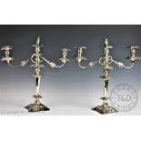 A large pair of silver plated candelabra, cast with foliate motifs, on serpentine square bases,
