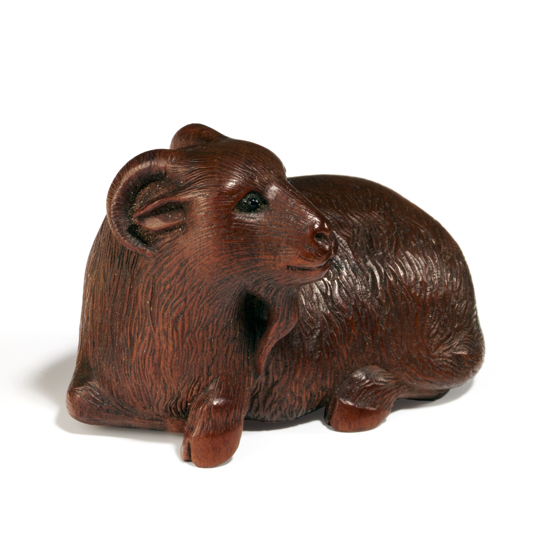 NETSUKE: LIEGENDE ZIEGE. Japan. Meiji-Zeit. Frühes 20. Jh. Dunkles Holz, Augen und himotoshi aus