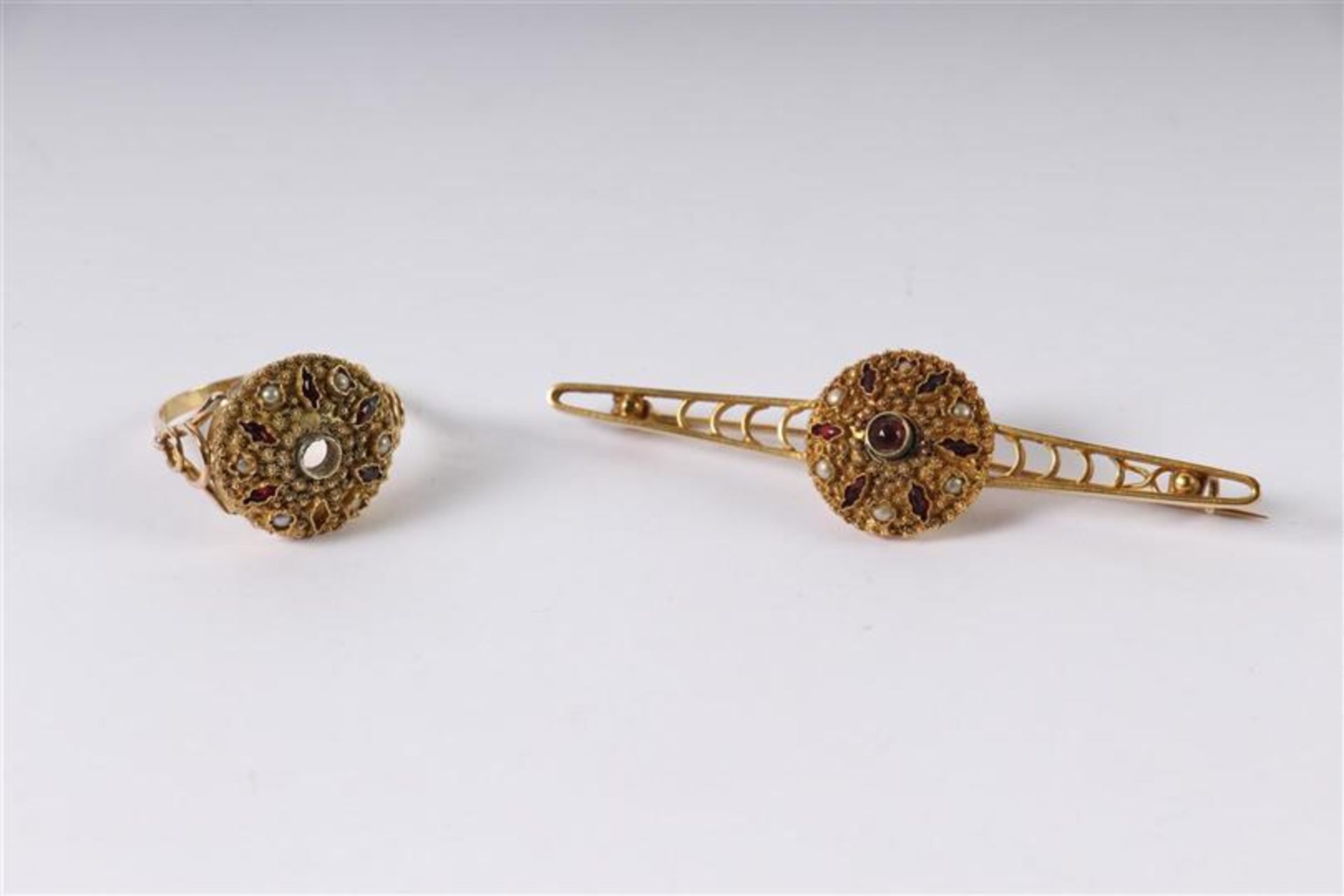 Gouden staafbroche bezet met rode steentjes en zaadparels en een dito bijpassende ring (steentje
