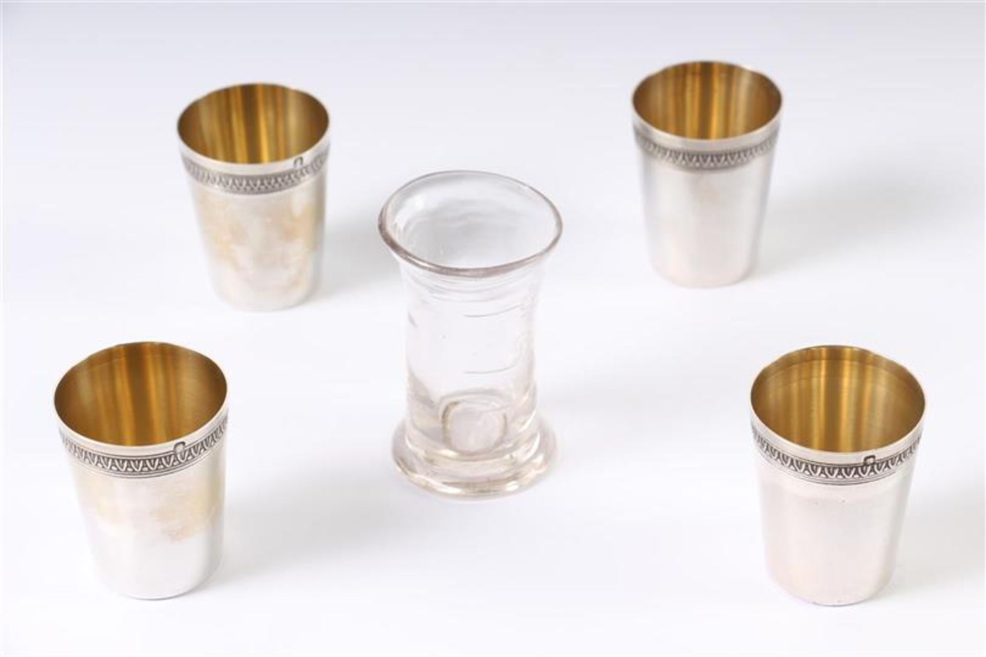 Vier zilveren shotglaasjes, Frans gekeurd en een handgeblazen glazen maatglaasje. H: 4 en 6 cm.
