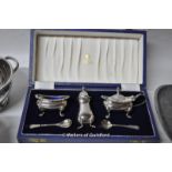 Silver: cruet set, cased, four decanter labels, two napkin rings, 255g; a white metal dish with