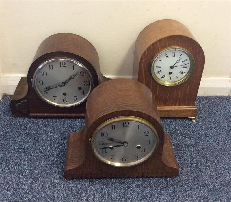 A group of three oak mantle clocks with dome tops.