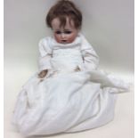 A German porcelain headed doll dressed in christen