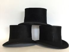 A group of three black top hats. Varying makers an