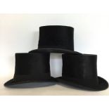 A group of three black top hats. Varying makers an