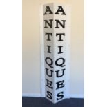 A large metal sign for "Antiques" in white with bl