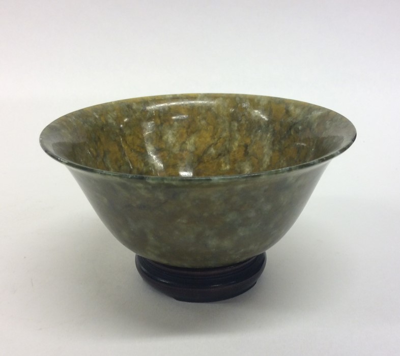 A small circular jade tea bowl on hardwood base. E