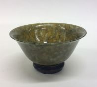 A small circular jade tea bowl on hardwood base. E