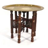 An Eastern tray table, the brass tray resting on a hardwood and mother-of-pearl inlaid folding base,