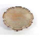 An early 20th century silver salver of circular form with piecrust border on four scroll feet,