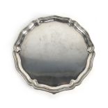 An early 20th century silver salver of circular form with piecrust border on three hoof feet,