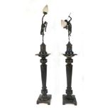 A pair of ebonised torchere stands holding a pair of spelter figural lamps with glass shades of